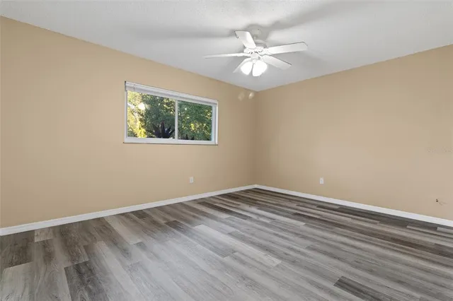 a view of an empty room with wooden floor and a chandelier fan