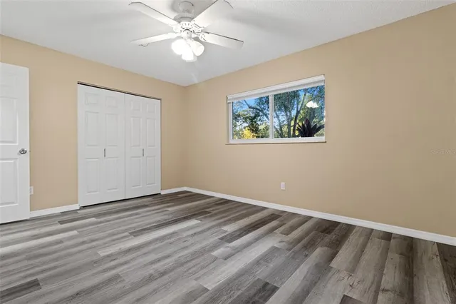 a view of an empty room with wooden floor and a ceiling fan