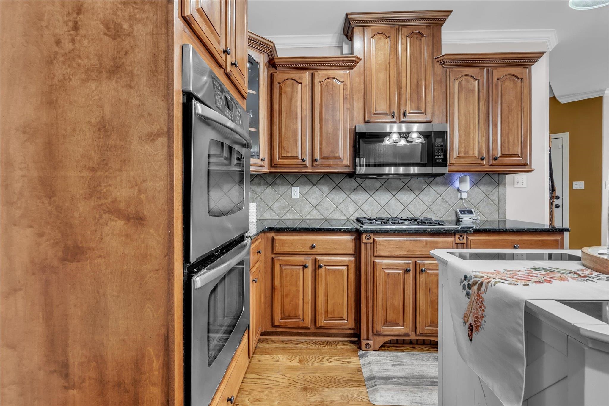 7284 Bucknell Road Millington, TN 38053 - Photo 13 of 35 Built-in stainless steel double ovens, gas cooktop, microwave, wood-finish cabinetry, and dark countertops