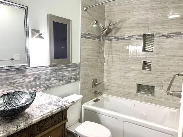 a bathroom with a granite countertop bathtub sink vanity mirror and toilet