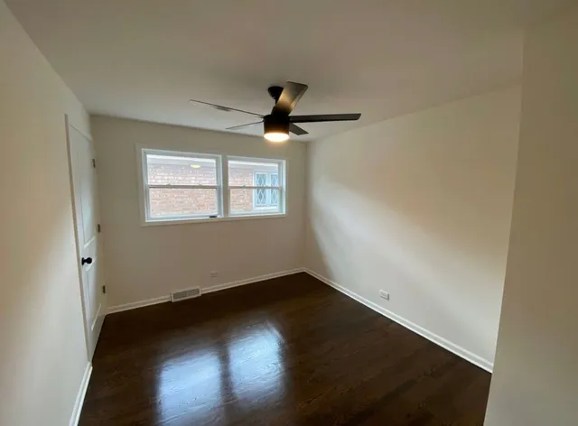 a view of an empty room with wooden floor and a ceiling fan