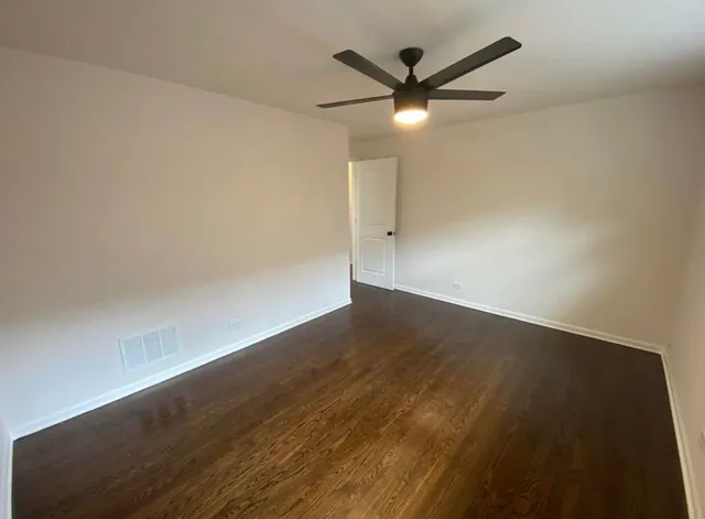 an empty room with wooden floor fan and windows