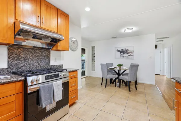 a kitchen with stainless steel appliances granite countertop a stove top oven a sink a dining table and chairs with wooden floor