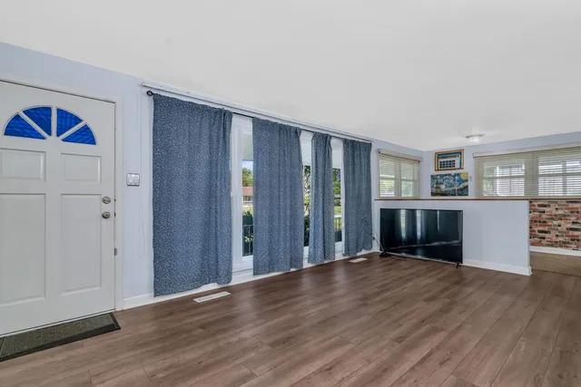 a view of an empty room with wooden floor and a kitchen