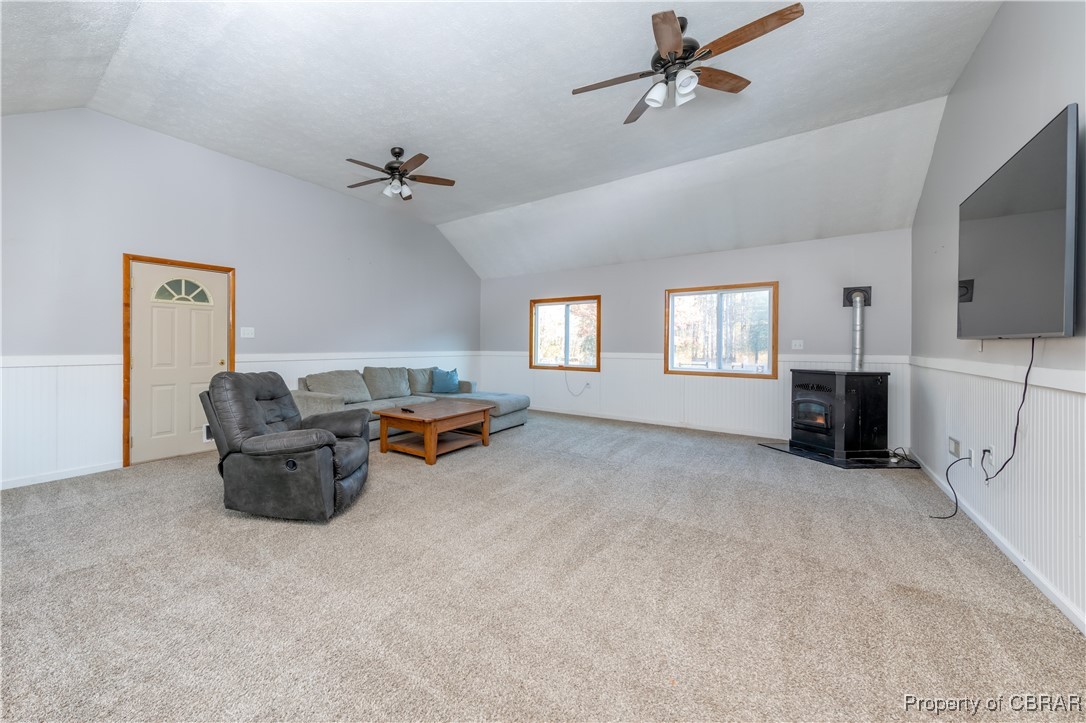 9534 Gee Farm Road Gloucester, VA 23061 - Photo 11 of 48 Carpeted living room with ceiling fan, a textured ceiling, lofted ceiling, and a wood stove