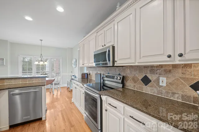 a kitchen with stainless steel appliances granite countertop white cabinets and a stove top oven
