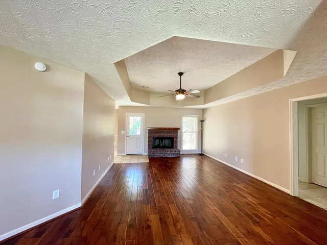 a view of an empty room with wooden floor fireplace and a window