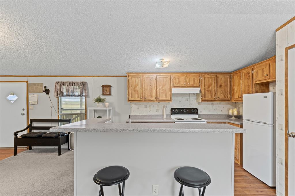 167 Hcr 4105 Covington, TX 76636 - Photo 19 of 32 Kitchen featuring white appliances, light countertops, under cabinet range hood, a breakfast bar area, and a textured ceiling