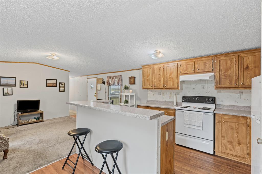 167 Hcr 4105 Covington, TX 76636 - Photo 20 of 32 Kitchen with white appliances, under cabinet range hood, wood finished floors, a kitchen bar, and light countertops