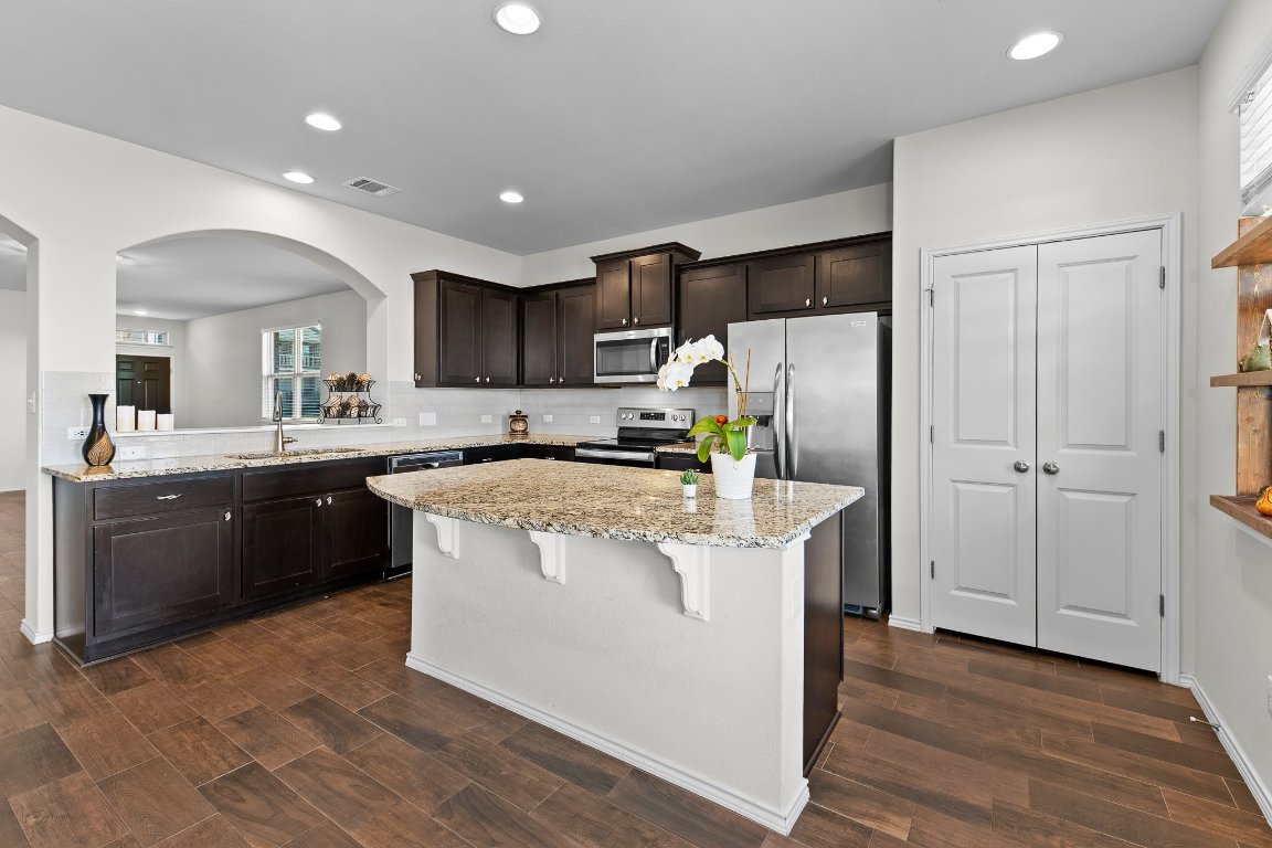 704 Coltrane Drive Pflugerville, TX 78660 - Photo 14 of 39 a kitchen with stainless steel appliances granite countertop a refrigerator a sink dishwasher a stove top oven a large island with wooden floor and cabinets