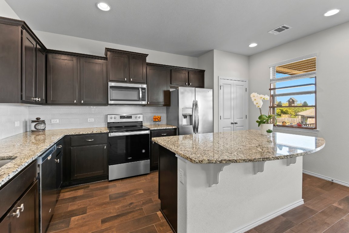 704 Coltrane Drive Pflugerville, TX 78660 - Photo 15 of 39 a kitchen with stainless steel appliances granite countertop a stove a sink dishwasher a refrigerator and a oven with wooden floor