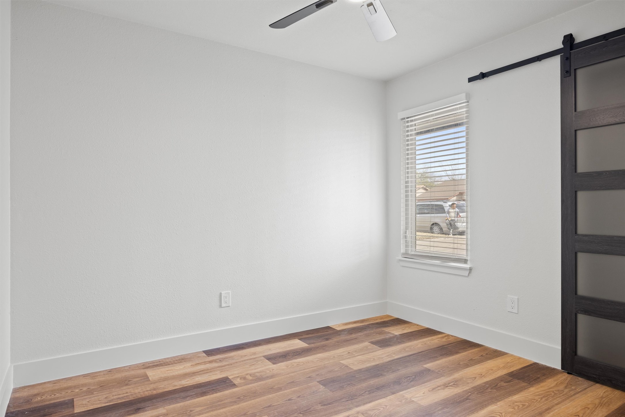 6212 Boxcar Run Austin, TX 78745 - Photo 24 of 36 Unfurnished bedroom with a barn door, wood finished floors, and ceiling fan