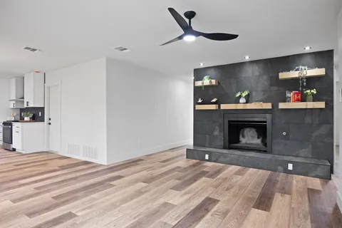 a view of a livingroom with a fireplace a ceiling fan and wooden floor