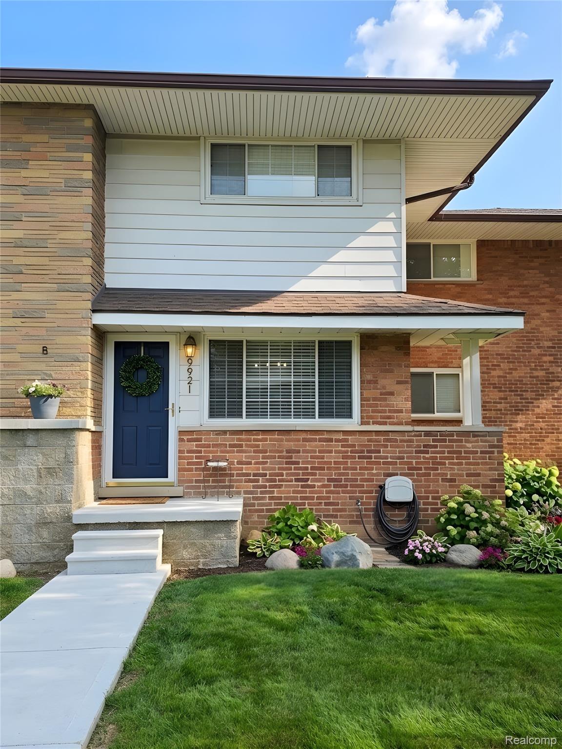 9921 Middlebelt Road, Unit 32 Livonia, MI 48150 - Photo 1 of 11 Split-level exterior featuring a deep blue entry door, brick and horizontal siding finishes, concrete front steps, and an established garden bed with varied plantings