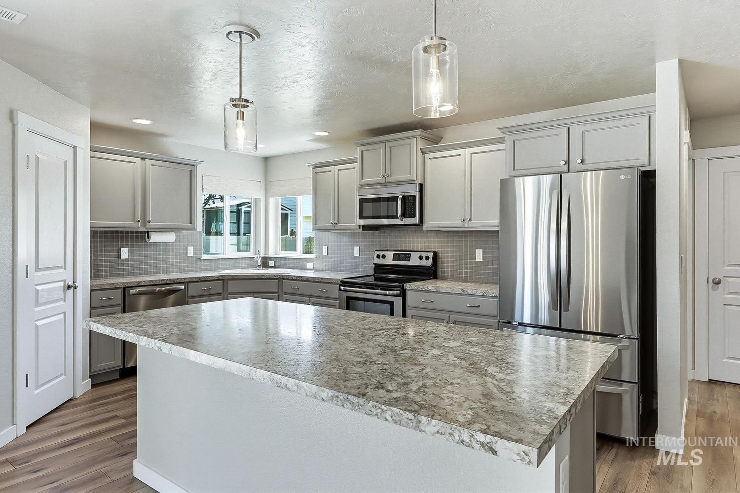 846 North Hidden View Way Star, ID 83669 - Photo 10 of 49 Kitchen featuring a large island with stone-finish countertop, stainless steel appliances, shaker-style cabinetry, square tile backsplash, and wood-finish flooring