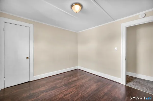 a view of an empty room with wooden floor and a fan
