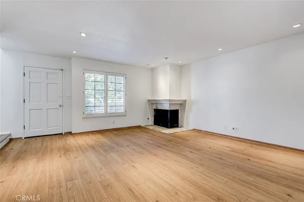an empty room with wooden floor fireplace and windows