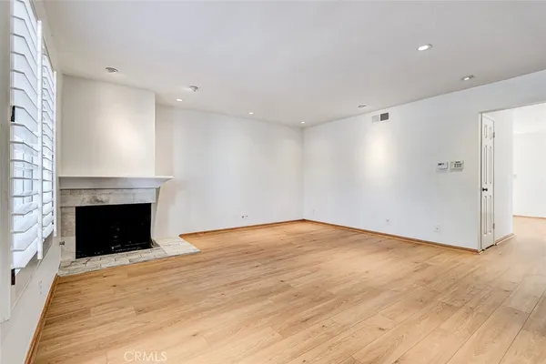 a view of an empty room with wooden floor fireplace and a window