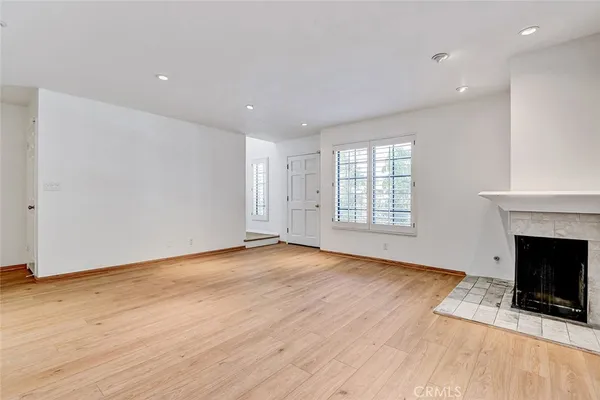 a view of an empty room with wooden floor fireplace and a window