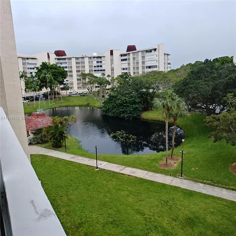 a view of a lake with a big yard and a large building with a large tree in the background