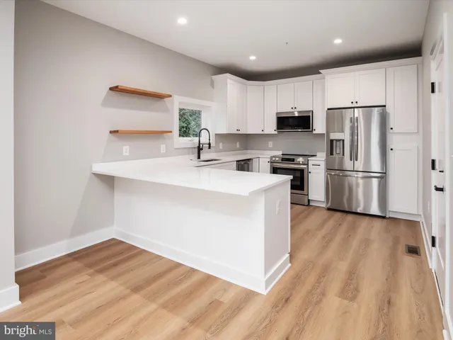 a kitchen with stainless steel appliances a sink dishwasher a refrigerator and a stove with wooden floor