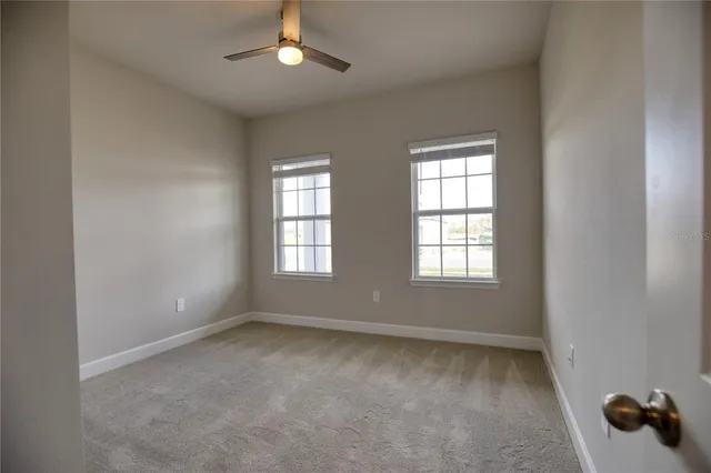 an empty room with chandelier fan and windows