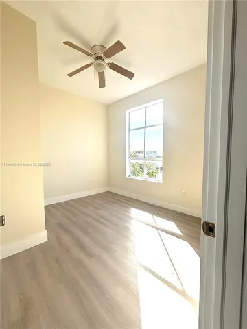an empty room with wooden floor fan and windows