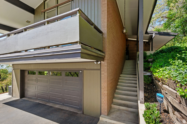 1900 North 100 East Provo, UT 84604 - Photo 3 of 49 Property entrance featuring an attached garage with panel door and upper window inserts, an exterior brick wall, and a concrete staircase with a wood railing leading to the upper level