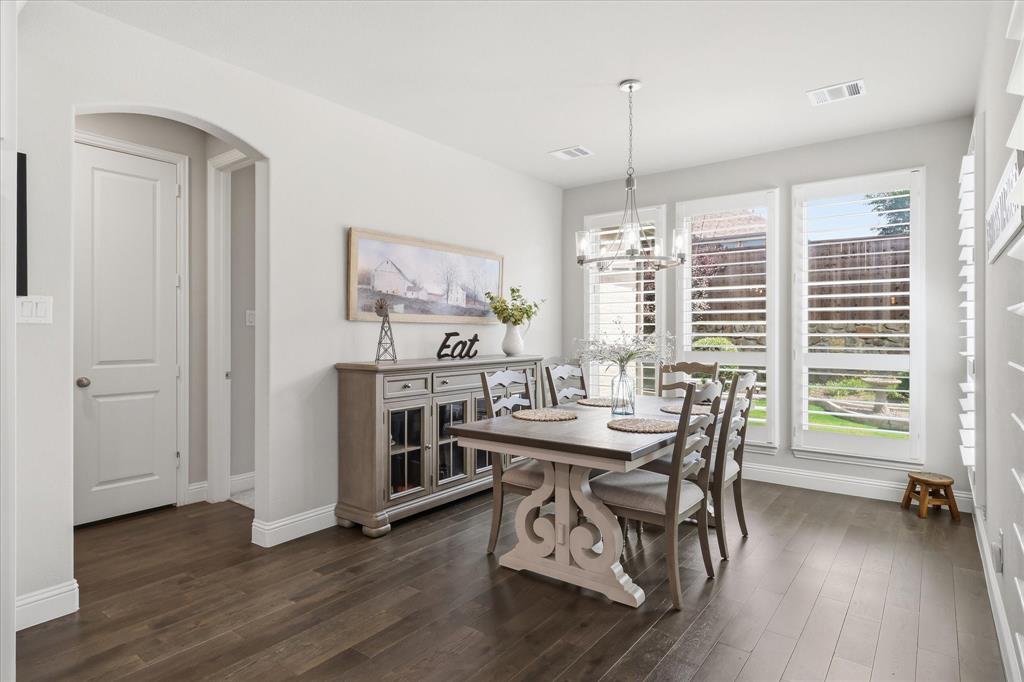 9708 Surveyor Road Oak Point, TX 75068 - Photo 7 of 34 Dining area featuring dark wood-finish flooring, white plantation shutters, and a contemporary chandelier