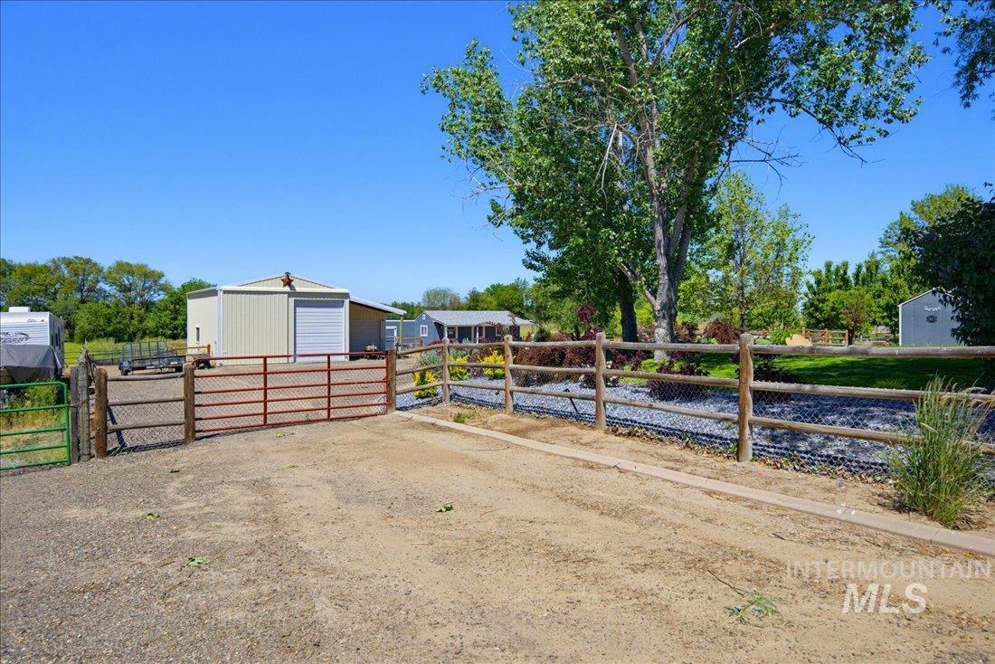24623 Falcon Lane Caldwell, ID 83607 - Photo 31 of 40 Gravel driveway with a red metal gate, leading to a beige metal building with a white overhead door