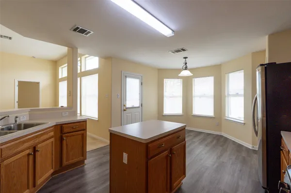 a large kitchen with kitchen island granite countertop a stove a sink a refrigerator and white cabinets with wooden floor