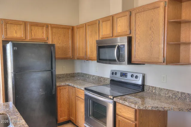 a kitchen with stainless steel appliances granite countertop a refrigerator a stove a sink and dishwasher with wooden cabinets