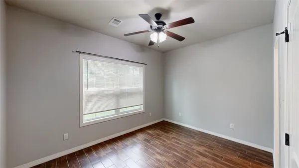 an empty room with wooden floor chandelier fan and windows
