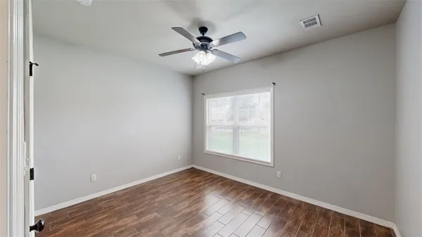 an empty room with wooden floor fan and windows