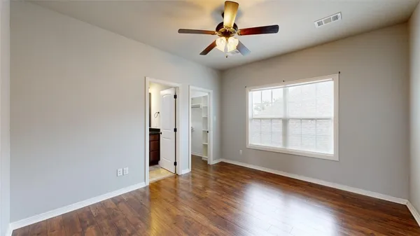 an empty room with wooden floor chandelier fan and windows