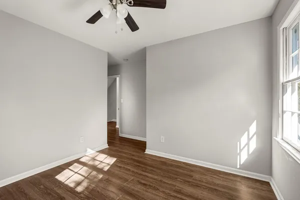an empty room with wooden floor chandelier fan and windows