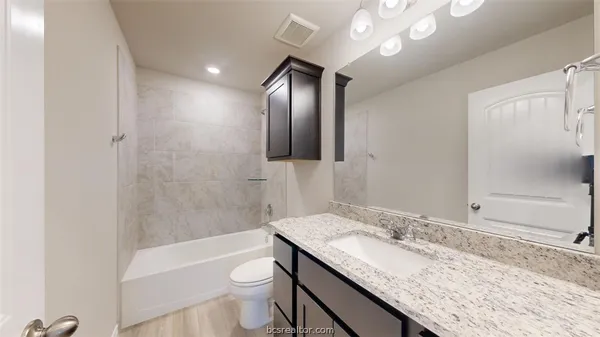 a bathroom with a granite countertop sink toilet mirror and bathtub