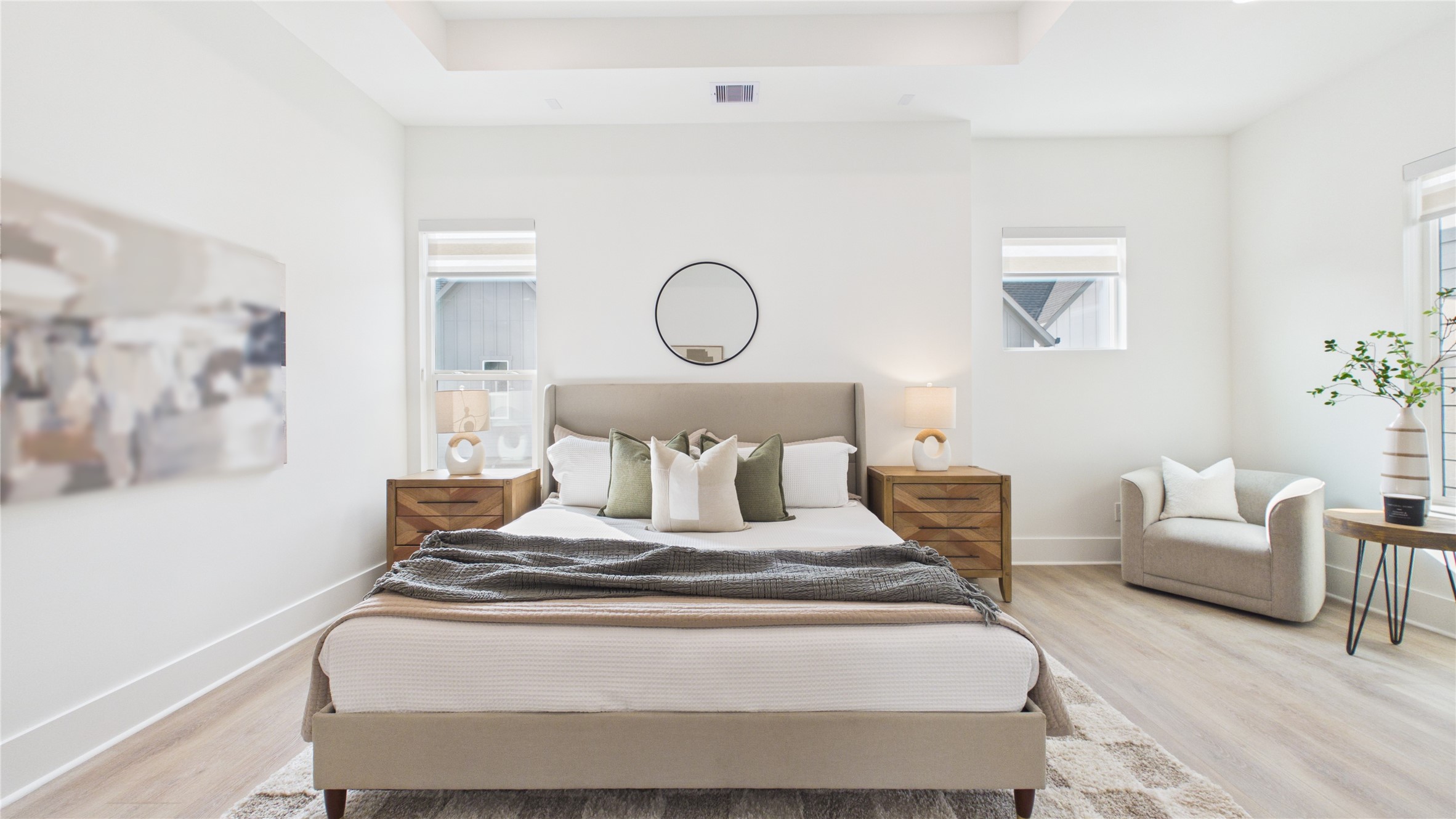 602 Skyland Terrace Way Houston, TX 77009 - Photo 26 of 40 This is a bright, modern bedroom featuring a comfortable bed with neutral bedding, two wooden nightstands with lamps, and a cozy armchair. The room is accented with minimalist decor and natural light from two windows, creating an inviting atmosphere.