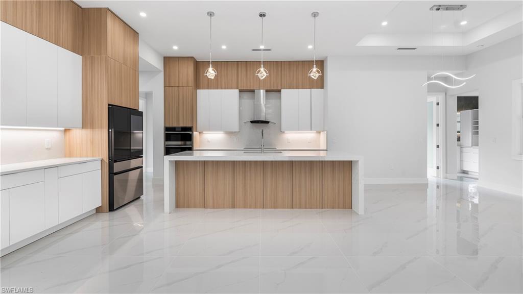 1687 19th Street Southwest Naples, FL 34117 - Photo 49 of 50 Kitchen featuring modern cabinets, open floor plan, a raised ceiling, brown cabinets, and hanging light fixtures