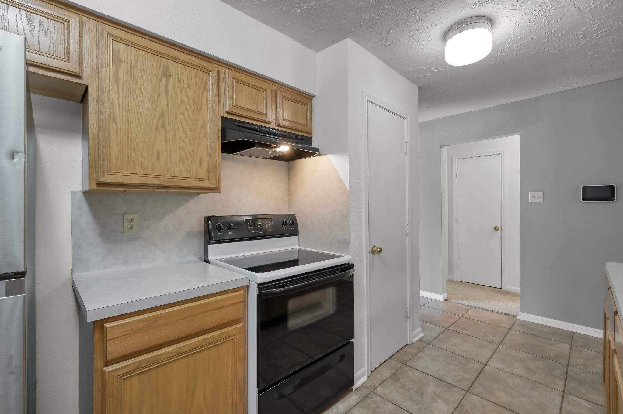 4314 Enchantedgate Drive Spring, TX 77373 - Photo 15 of 47 Kitchen features a modern electric stove and stainless steel appliances, complemented by light wood cabinets and neutral countertops. The space is bright with a tiled floor and has easy access to adjacent rooms.