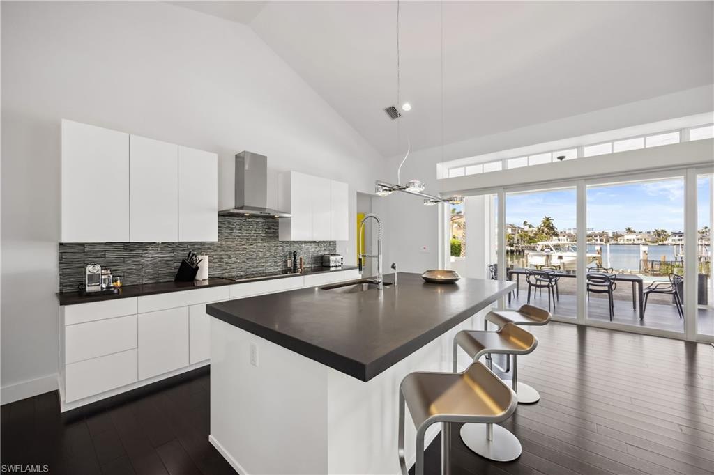 299 Mermaids Bight Naples, FL 34103 - Photo 8 of 28 a kitchen with stainless steel appliances granite countertop a sink a stove and chairs with wooden floor