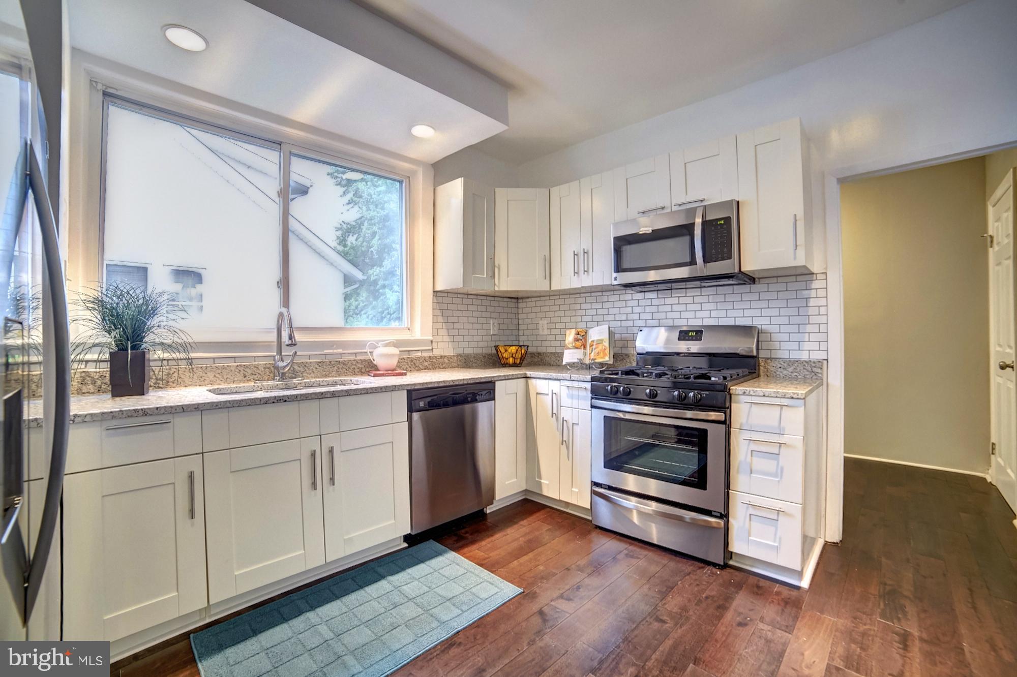 a kitchen with stainless steel appliances granite countertop a sink a stove a microwave a refrigerator a window and cabinets