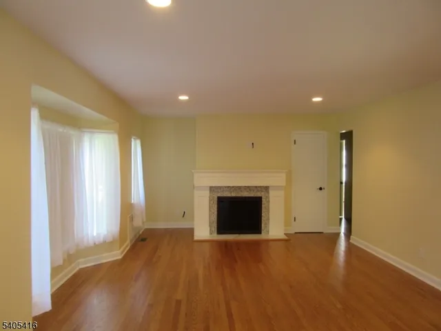 a view of an empty room with wooden floor fireplace and a window