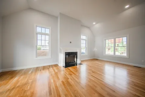 an empty room with wooden floor fireplace and windows