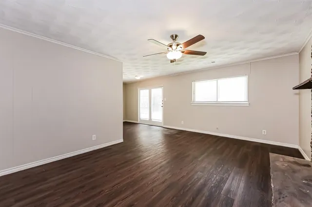 an empty room with wooden floor fan and windows