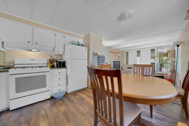 a kitchen with stainless steel appliances kitchen island granite countertop a stove a refrigerator a dining table and chairs with wooden floor