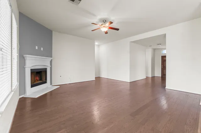 a view of an empty room with wooden floor fireplace and a window