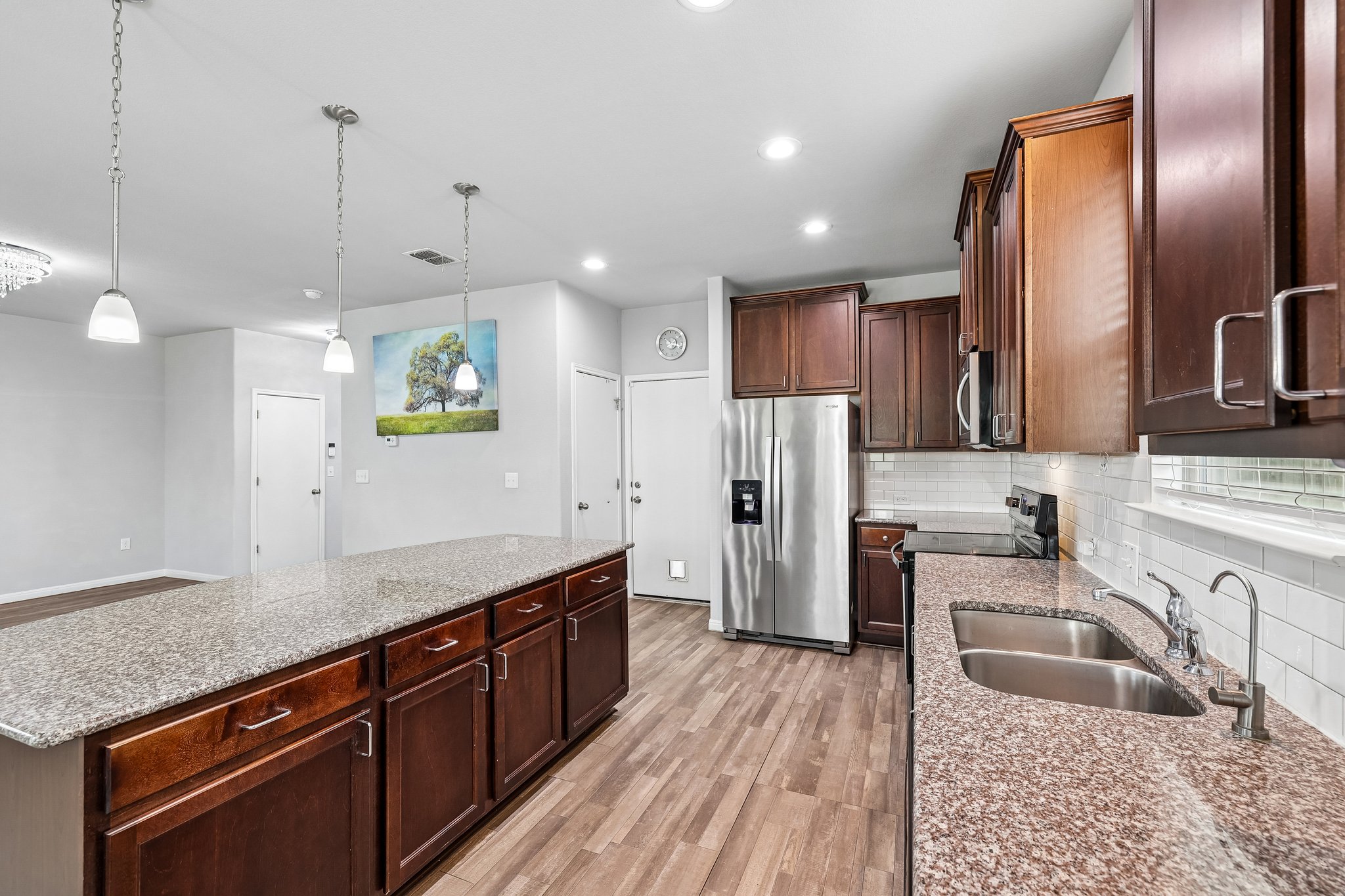 387 Guemal Road Buda, TX 78610 - Photo 11 of 39 Kitchen featuring granite countertops, wood-finish flooring, stainless steel appliances, dark wood cabinetry, and a subway tile backsplash