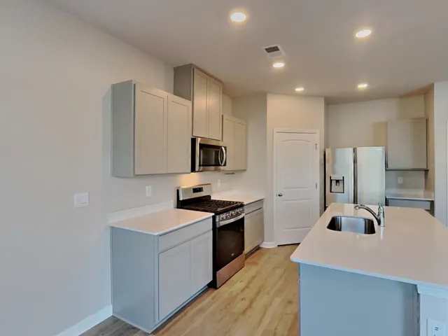 a kitchen with stainless steel appliances a stove top oven a sink a refrigerator and white cabinets