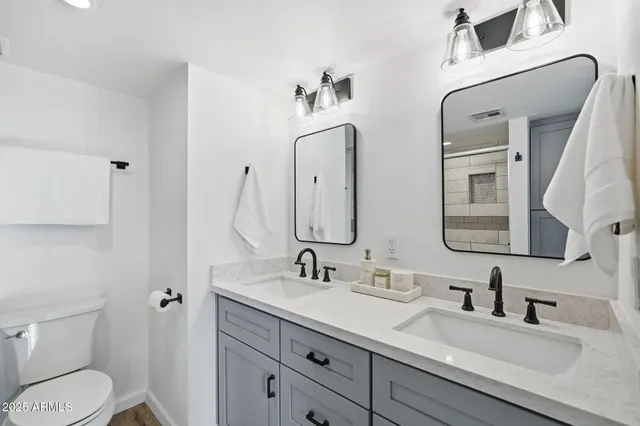 a bathroom with double vanity sink a toilet and a mirror